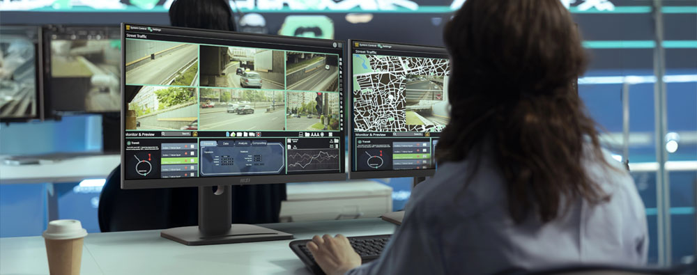 A government official overseeing live road monitoring systems on a business desktop computer with multiple displays.