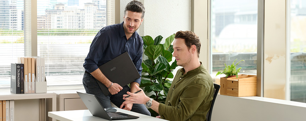 An office scene of a small to medium-sized enterprise, showing two employees using laptops.